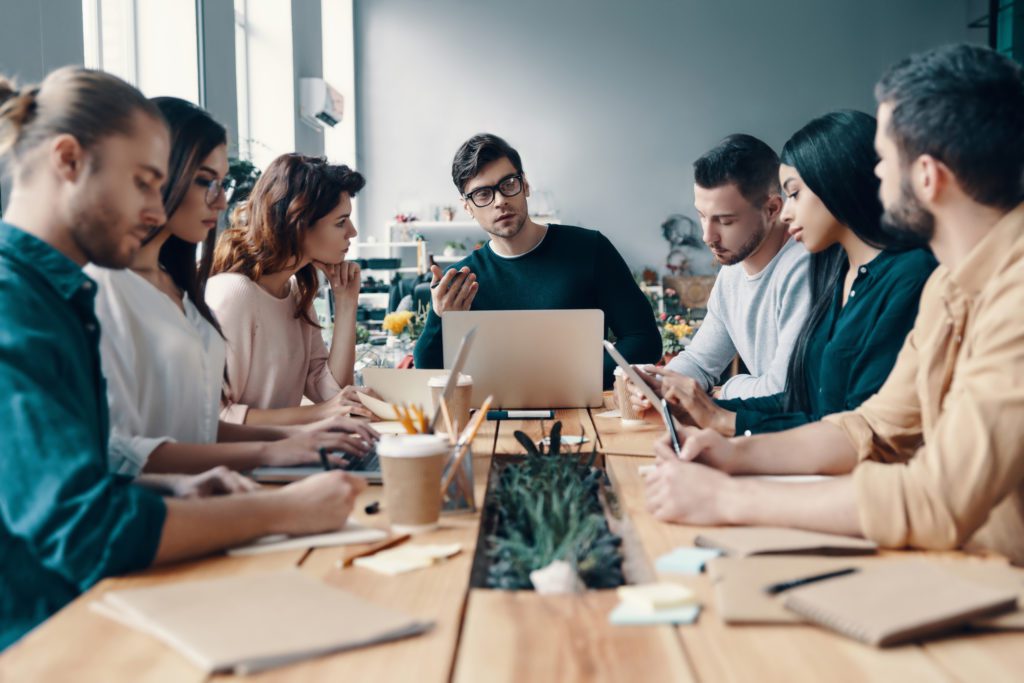 Leader of a group sits at the head of a table, surrounded by his team
